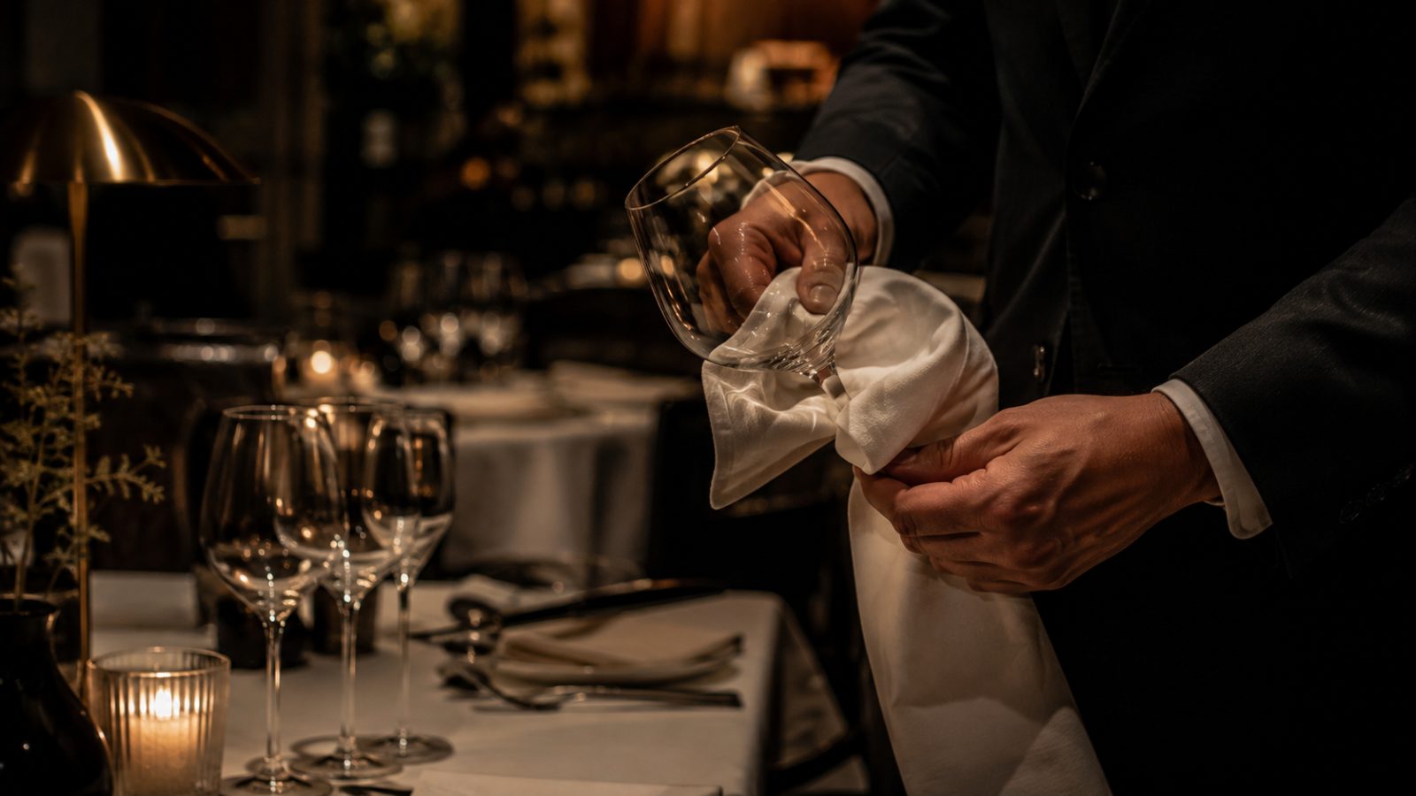 Server polishing a wine glass at a candlelit table